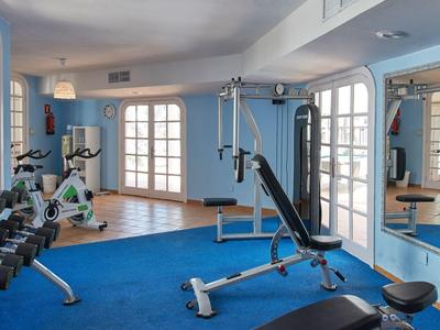 Salle de sport lumineuse avec divers équipements d'entraînement et moquette bleue.