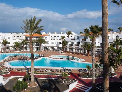 Hôtel avec bâtiment blanc et piscine, entouré de palmiers et de chaises longues.