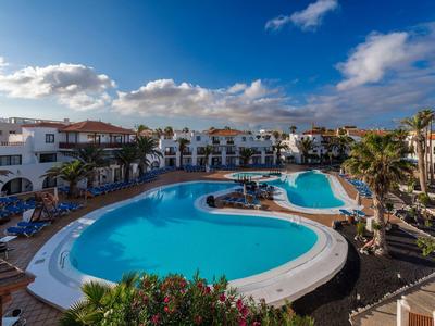 Grande piscina all'aperto in un complesso alberghiero con cielo blu e edifici bianchi.