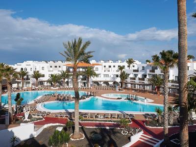 Hotel z białym budynkiem otaczającym duży basen i palmami pod czystym niebem.