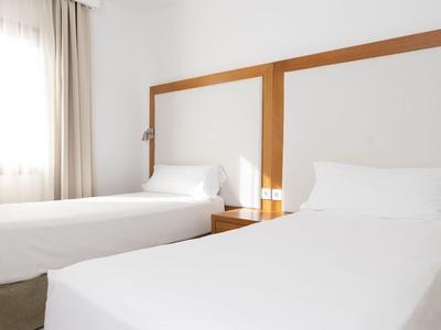 Jasny pokój hotelowy z dwoma pojedynczymi łóżkami i prostymi drewnianymi zagłówkami.