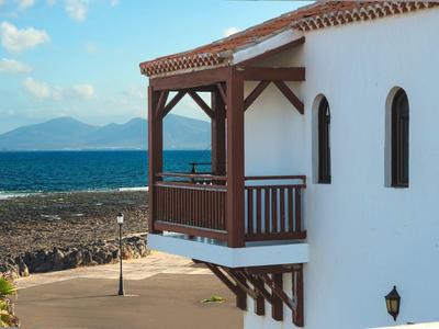Drewniany balkon na białym budynku z widokiem na morze i skaliste wybrzeże.