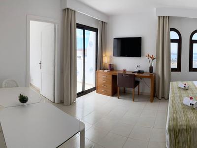 Jasny pokój hotelowy z podwójnym łóżkiem, biurkiem, telewizorem i balkonem z widokiem na zewnątrz.