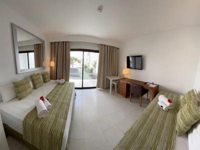 Jasny pokój hotelowy z dwoma łóżkami, biurkiem, telewizorem i dostępem do balkonu.