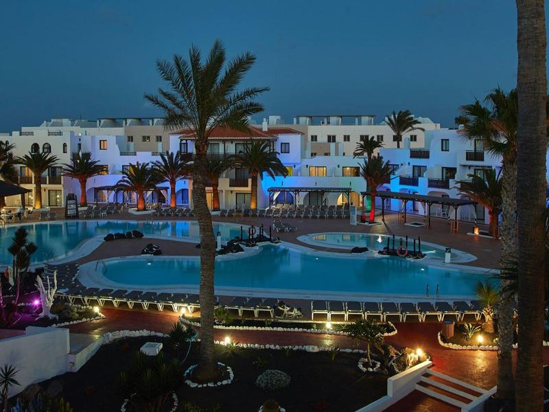 Oświetlony hotel z dużym basenem i palmami w nocy