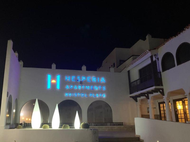 Widok zewnętrzny budynku nocą z podświetlonym logo hotelu.