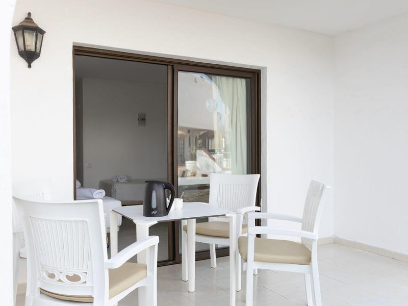 Biały balkon z czterema krzesłami i stołem przed przesuwnymi drzwiami ze szkła w hotelu.