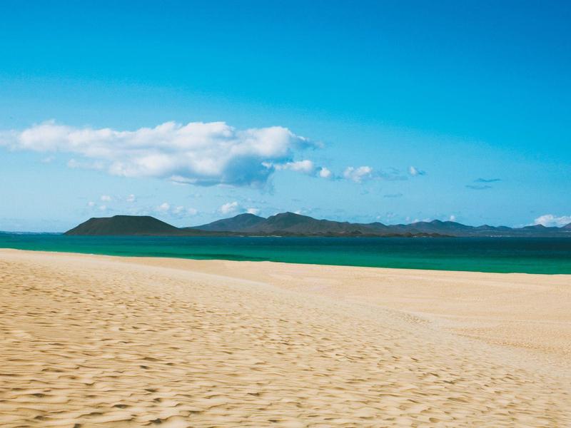 Pusta piaszczysta plaża z niebieskim niebem i zielonymi wyspami na horyzoncie.