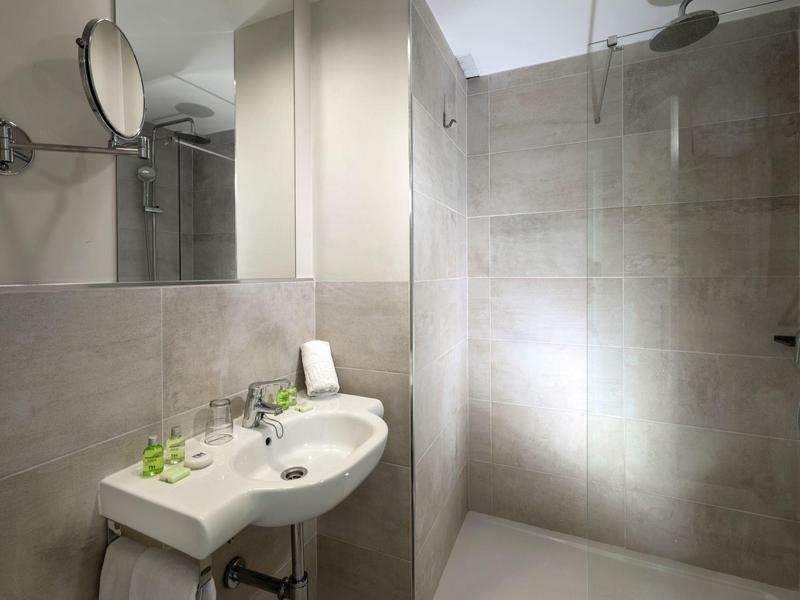 Nowoczesna łazienka z umywalką, lustrem i prysznicem typu walk-in w neutralnych kolorach.