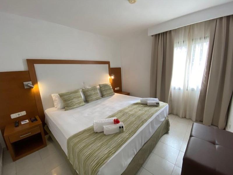 Jasny pokój hotelowy z łóżkiem podwójnym, zielonymi akcentami i starannie złożonymi ręcznikami.