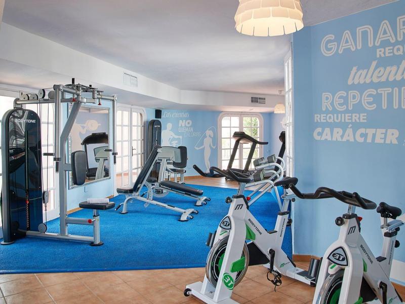 Nowoczesna siłownia hotelowa z różnorodnym sprzętem do ćwiczeń i jasnym wnętrzem.