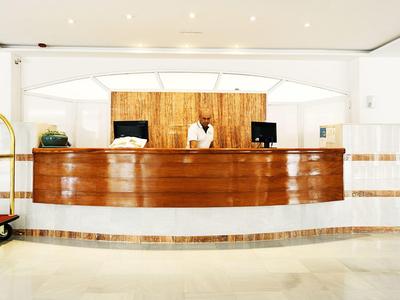 Moderner Hotel-Empfang mit weißem Ambiente, rundem Holzempfangstresen und Mitarbeiter dahinter.