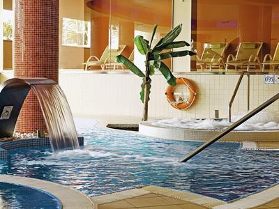Innen-Wellnessbereich mit blauem Whirlpool, Wasserfall, Pflanzen und ruhigen Sitzplätzen.