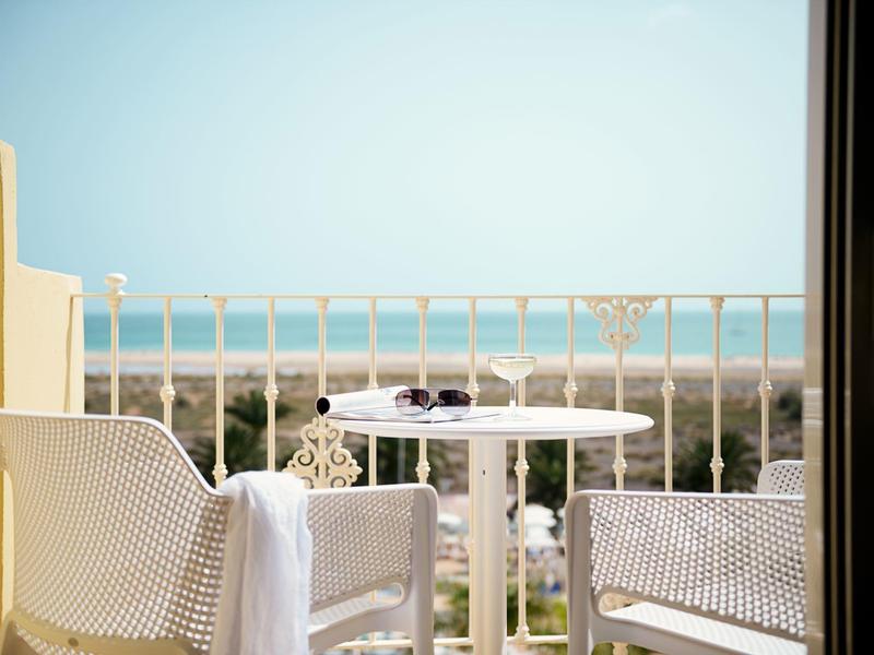 Sedie da patio bianche e un tavolo su un balcone con vista sulla spiaggia e sull'oceano.