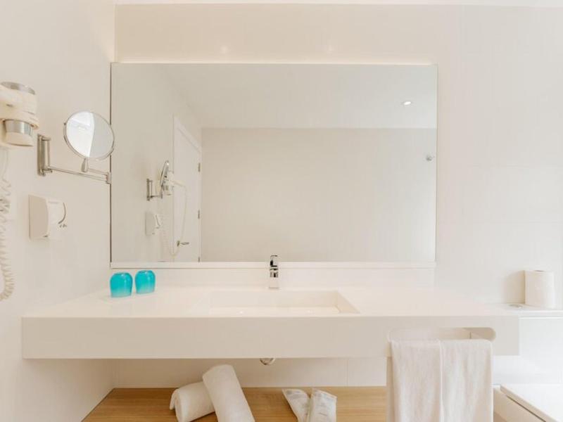Bagno bianco minimalista con lavabo, grande specchio, asciugamano e asciugacapelli a parete.