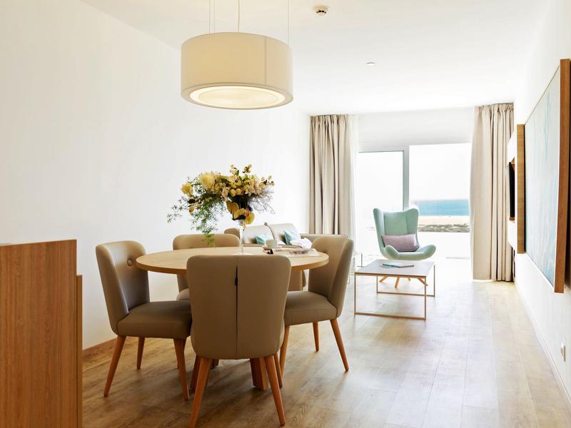 Zona pranzo luminosa con tavolo rotondo, sedie beige e vista sull'oceano dalla finestra.