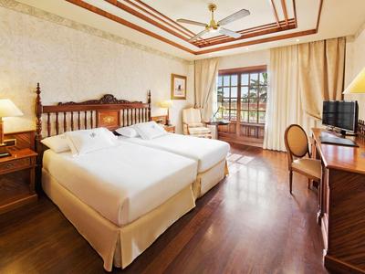 Světý hotelový pokoj se dvěma jednolůžky, dřevěným nábytkem a balkonem s výhledem ven.