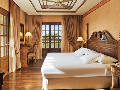 Pohodlný hotelový pokoj s dřevěným nábytkem, velkou postelí a výhledem na zahradu.