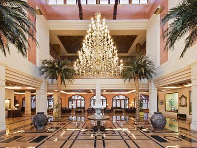 Velká hotelová lobby s lustrem, mramorovou podlahou a dekorativními palmami.