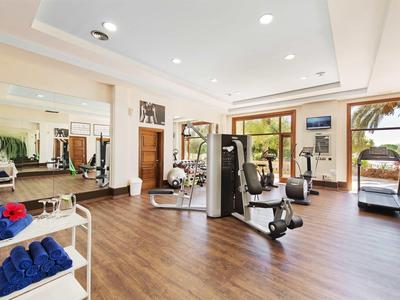 Heller Fitnessraum mit modernen Geräten, Holzfußboden und großen Fenstern mit Blick auf Palmen.