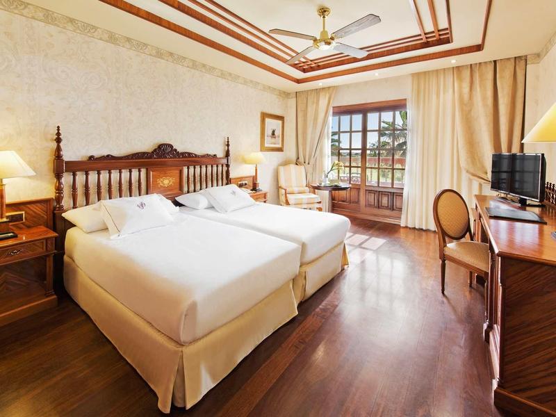 Světý hotelový pokoj se dvěma jednolůžky, dřevěným nábytkem a balkonem s výhledem ven.