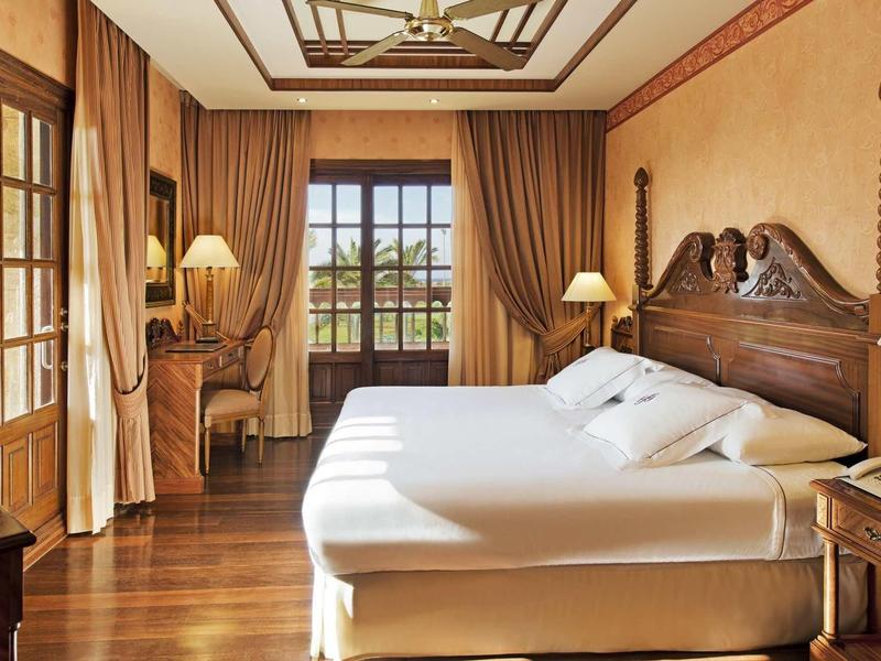 Pohodlný hotelový pokoj s dřevěným nábytkem, velkou postelí a výhledem na zahradu.