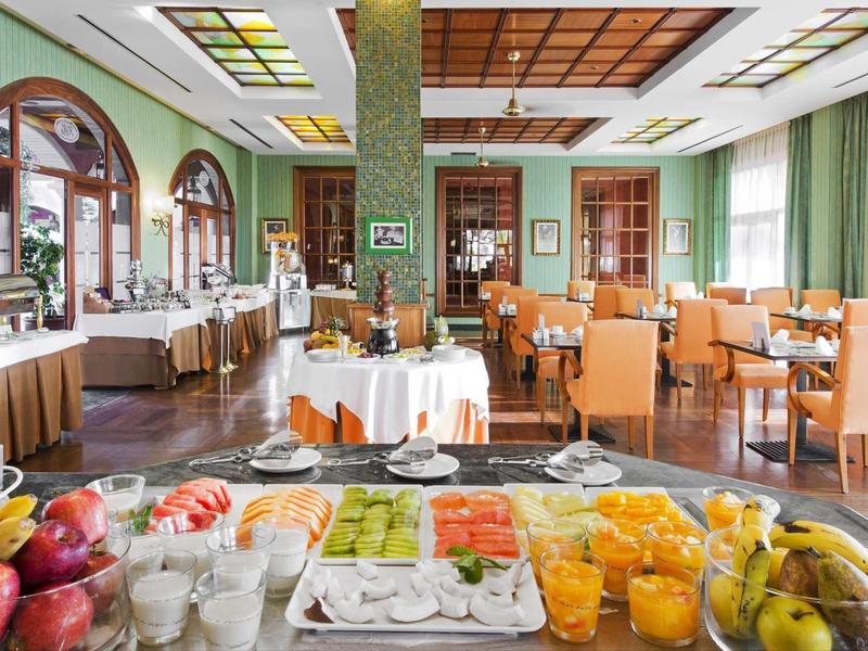 Světlá restaurace s různými stoly, židlemi a barevnými snídaňovými možnostmi na bufetu.