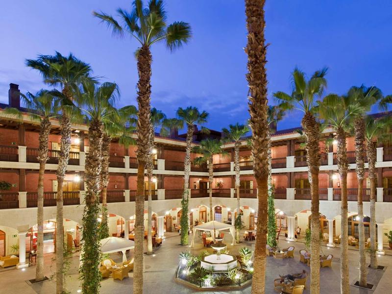 Hotelové nádvoří s palmami a fontánou za soumraku.