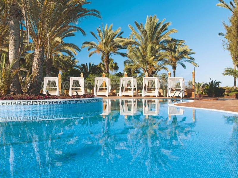 Příjemný bazén s lehátky a palmami pod jasnou modrou oblohou.