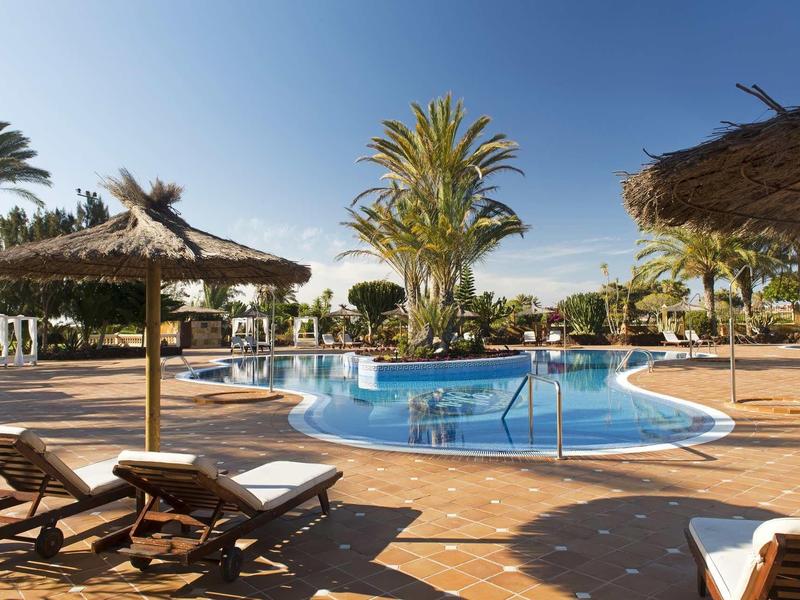 Otevřená oblast u bazénu s lehátky a palmami pod jasnou oblohou.