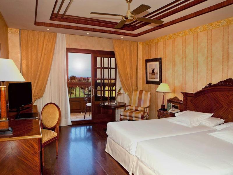 Hotelový pokoj se dvěma jednolůžky, dřevěným nábytkem a balkonem s výhledem ven.