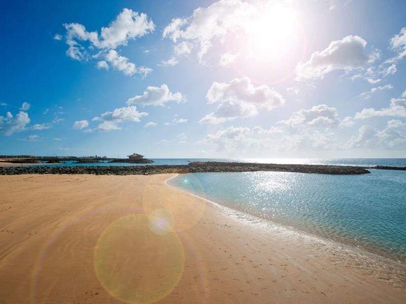 Playa soleada con agua azul clara y cielo ligeramente nublado en destino vacacional.