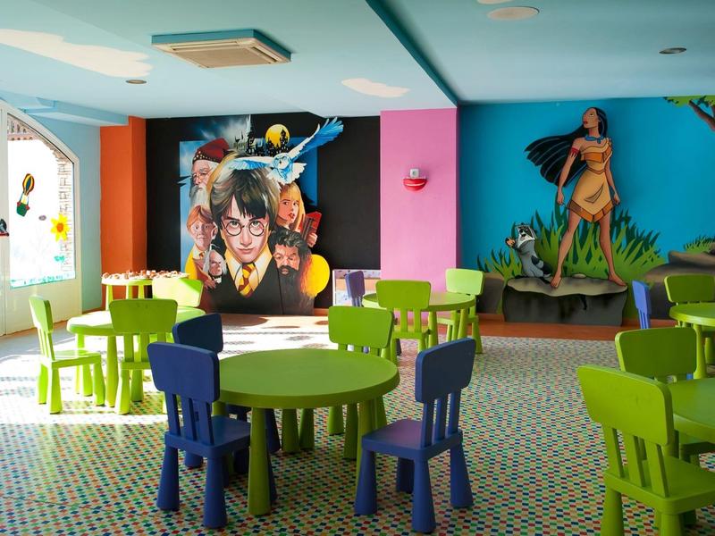 Sala de juegos colorida para niños con mesas, sillas y murales de personajes Disney.