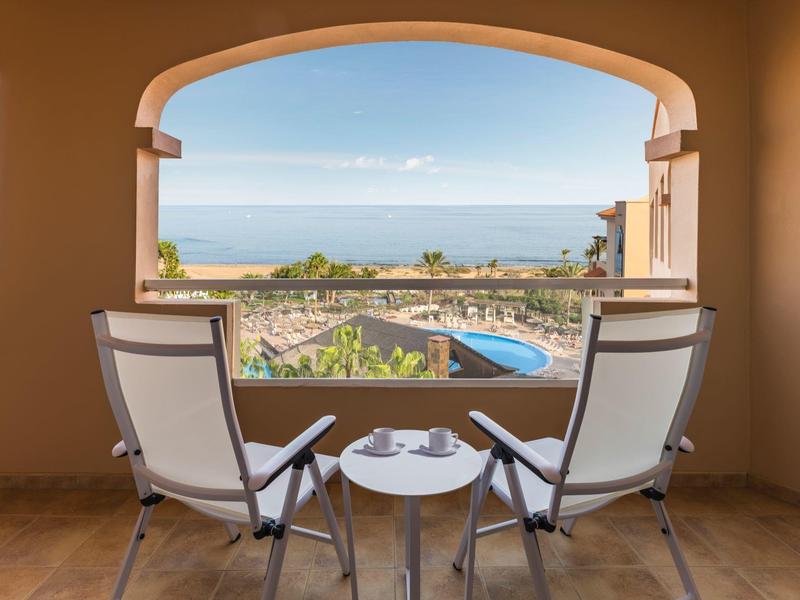 Vista desde una terraza con dos sillas y una mesa hacia una piscina y el mar al fondo.