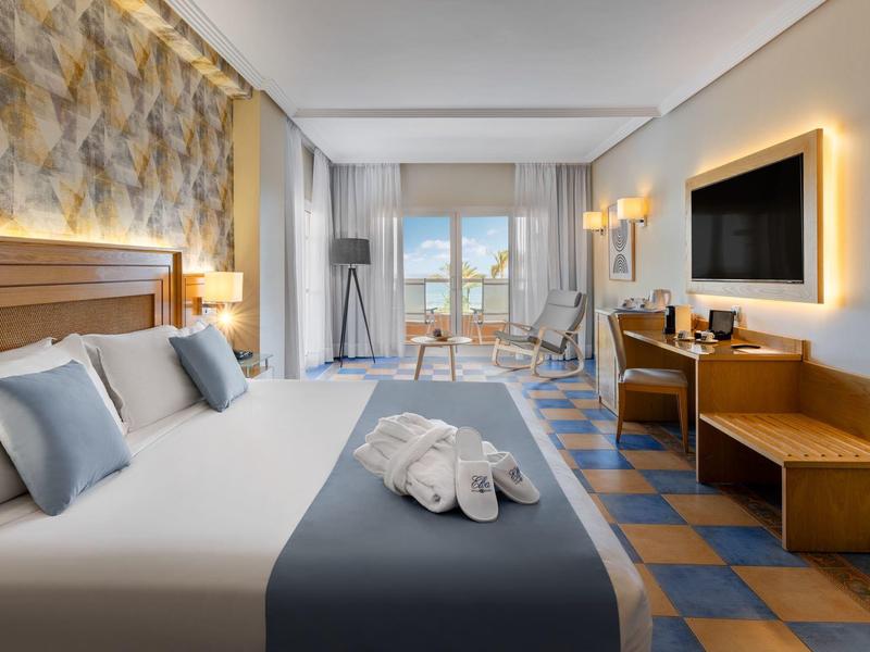 Habitación de hotel moderna con cama grande, televisor y escritorio, vista a la ciudad a través de la ventana.