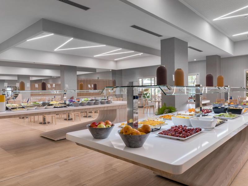 Área moderna de buffet de hotel con una variedad de alimentos en mostradores blancos y suelo de madera clara.