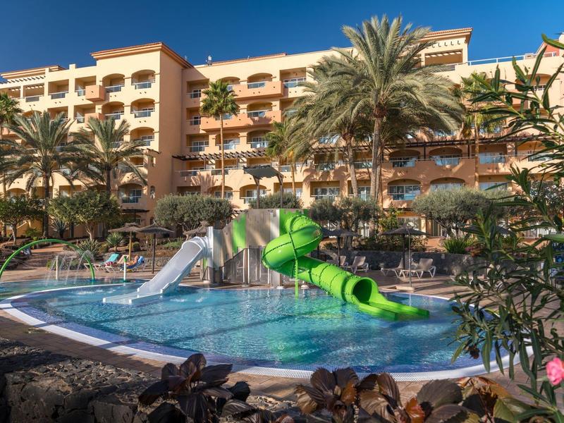 Piscina del hotel con toboganes y palmeras bajo un cielo azul claro.