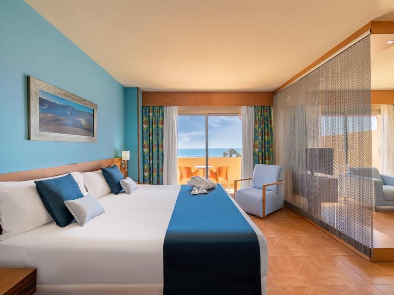 Modern hotelkamer met tweepersoonsbed, zithoek en uitzicht op zee door het raam.