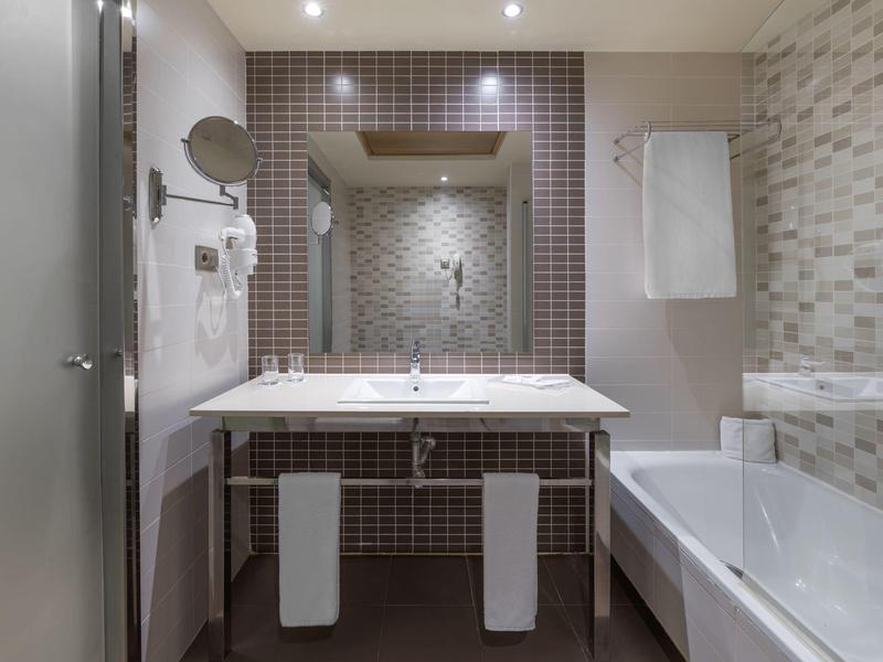 Lichte badkamer met dubbele wastafel, spiegel en badkuip in een hotel.