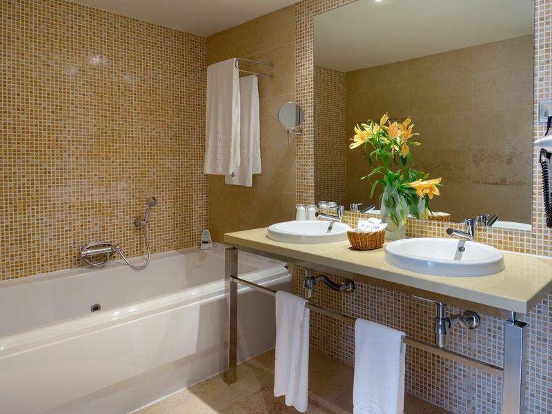 Moderne badkamer met bad, dubbele wastafels en bloemstuk.