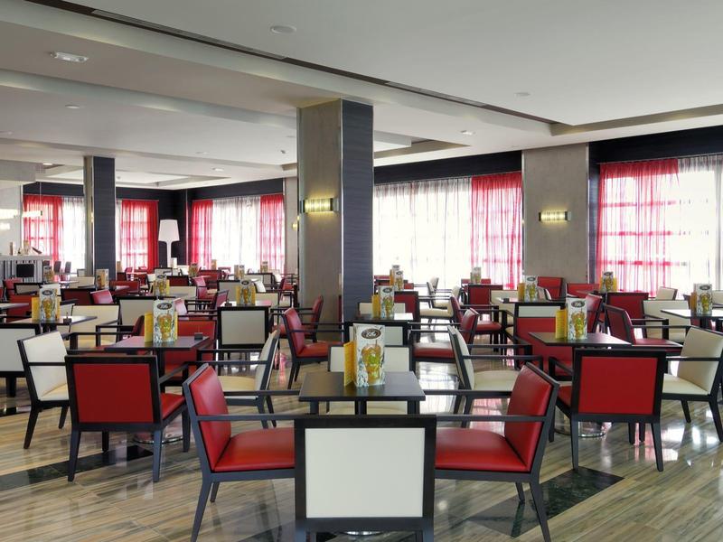 Ruim restaurant met rood-witte stoelen en grote ramen met rode gordijnen.