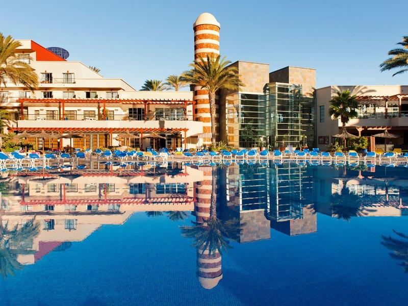 Hotel met groot zwembad en parasols onder een heldere blauwe lucht