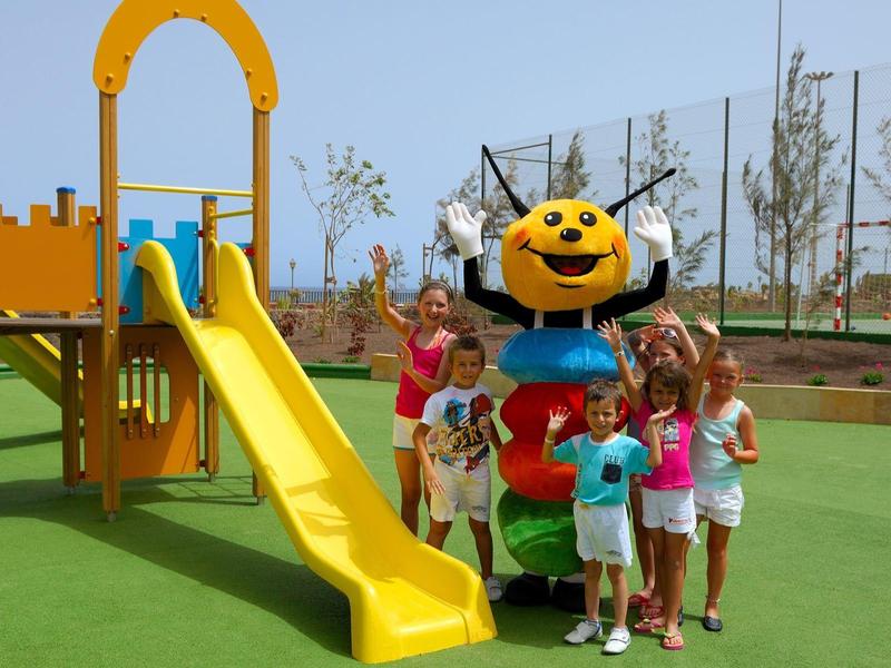 Kinderen spelen op een speeltuin met glijbaan naast een kleurrijk figuur.