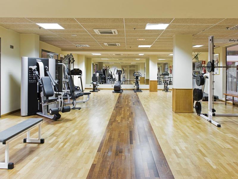 Lichte sportschool met houten vloer, spiegelwand en verschillende fitnessapparaten.