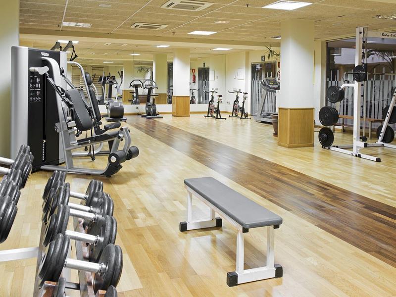 Lichte sportschool met diverse trainingsapparaten en halters op een houten vloer.