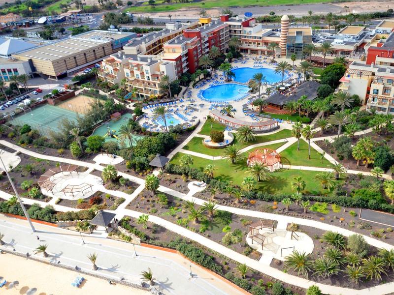 Groot resort met meerdere zwembaden, tuinen en woongebouwen naast een waterpark met glijbanen.