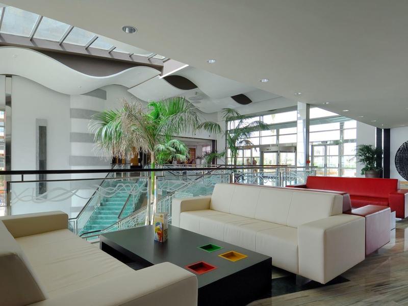 Lichte, moderne hotellobby met witte banken, glazen balustrade en veel daglicht.