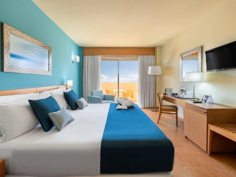 Modern hotelkamer met groot bed, blauwe accenten en zeezicht door het raam