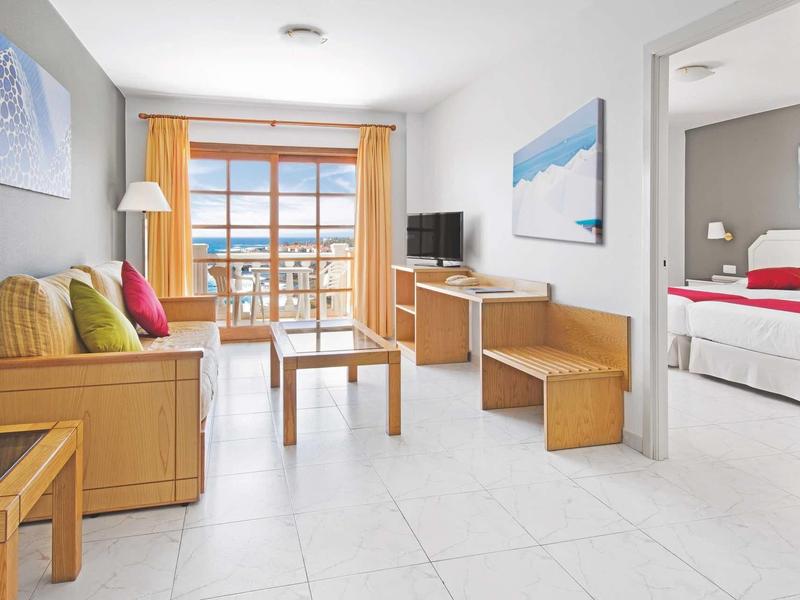 Světý a moderní obývací prostor s dřevěným nábytkem a výhledem na balkon a moře.