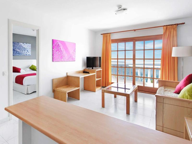 Pokoji hotelu s pohovkou, dřevěným nábytkem a balkonem s výhledem na moře.